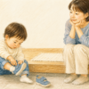 玄関で自分で靴を履こうとする2歳児を、そばで急かさず見守る大人のクレヨン画